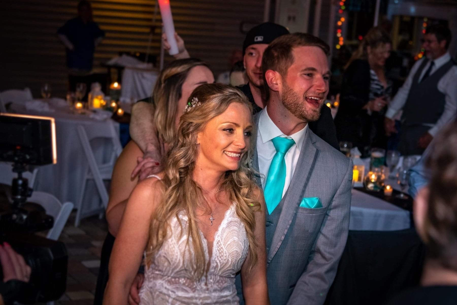 A bride and groom stand close together, smiling, at their warmly lit evening wedding reception.